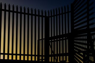 A gate and fencing with a blue/yellow sky in the background.